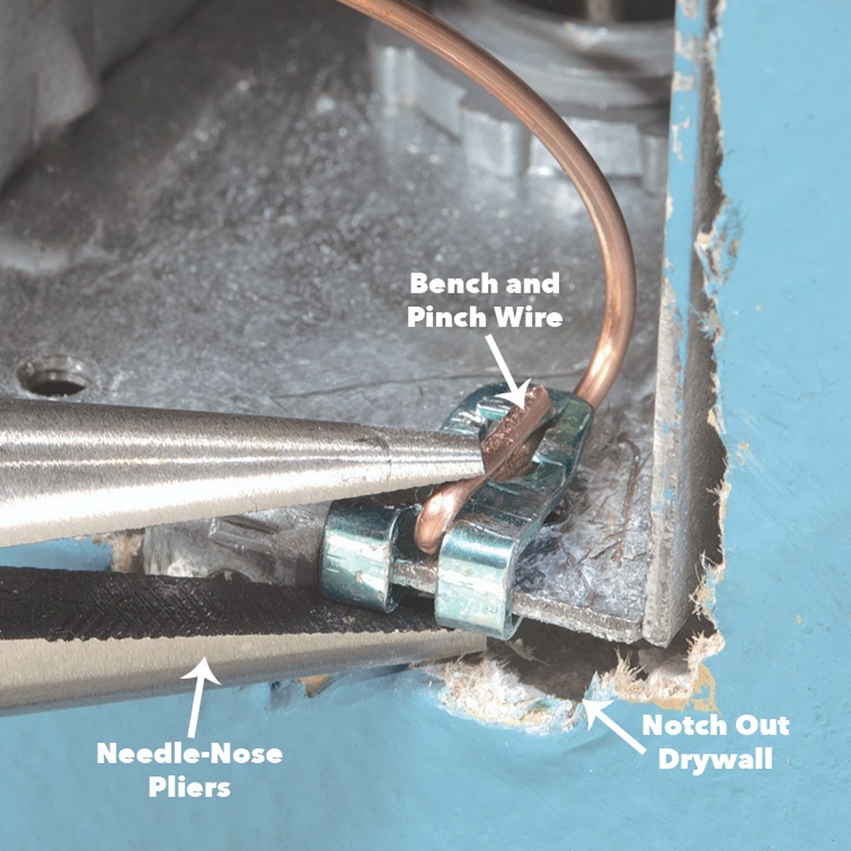 Needle-nose pliers pinch a copper wire, securing it against a metal bracket inside a notched drywall space, showing an electrical connection in progress.