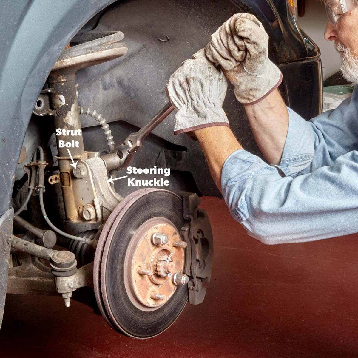A person uses a wrench to tighten a bolt on a car's suspension system within a garage, with parts labeled for clarity.