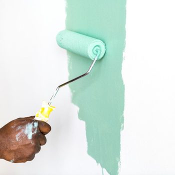 A hand holds a paint roller applying light green paint to a white wall, creating a fresh, vibrant contrast in an interior space.