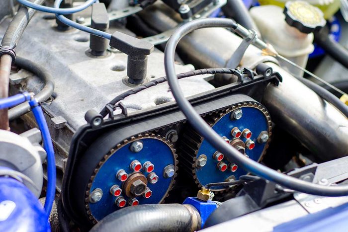 An engine component features blue gears connected by a black belt, surrounded by metallic parts and hoses in an automotive setting.