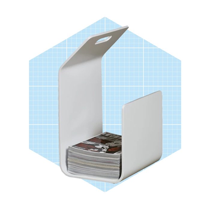 A white magazine holder displays stacked magazines inside while set against a light blue grid-patterned background.