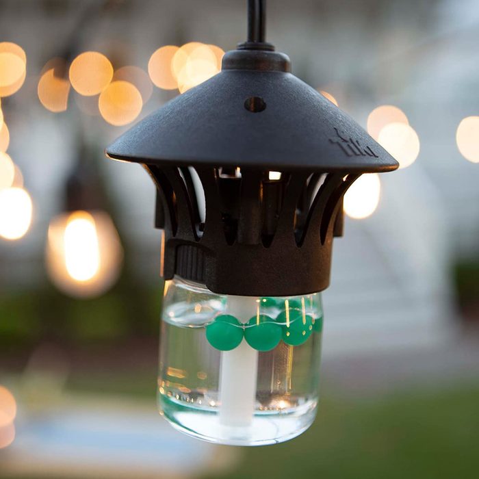 A hanging lantern with a black top contains water and green spheres inside a transparent glass container, glowing amidst blurred outdoor lights.