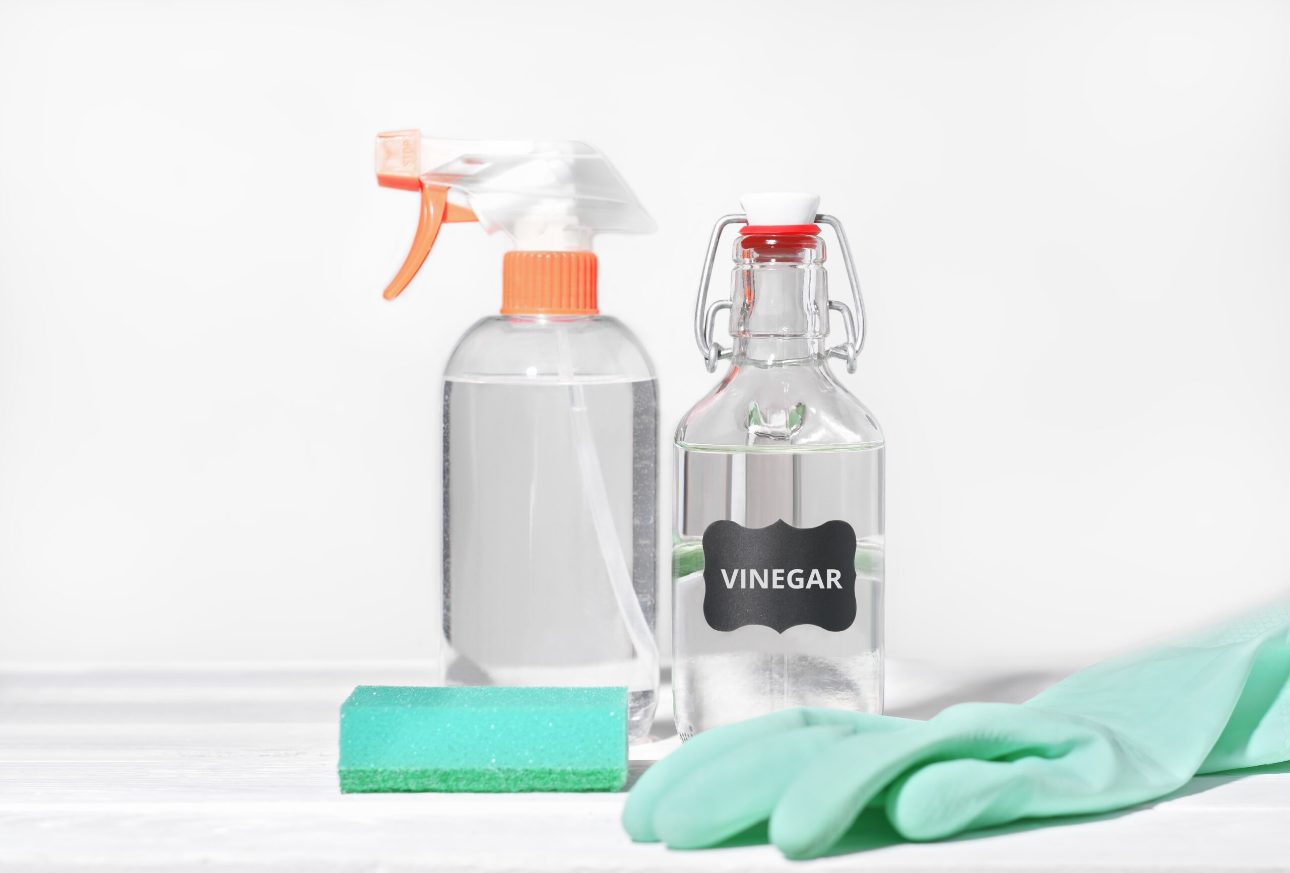 white vinegar for home cleaning chores, natural householding detergent, affordable product for housekeeping, rubber glove and kitchen sponge next to sprayer bottle.