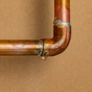 Copper plumbing pipe leaking water inside wall. Home repair, maintenance and remodeling concept.