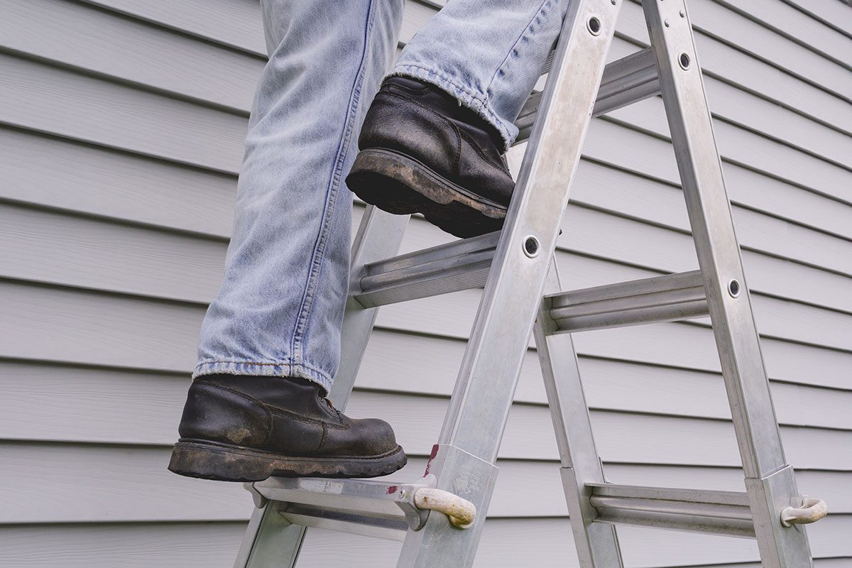 Male worker climbing stepladder in front of house siding