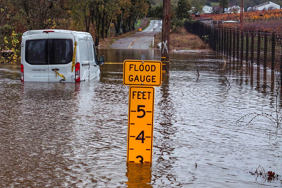 A small van sits stranded in floodwater with flood gauge in the middle